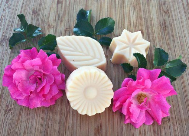 Rose lotion bars molded into leaf, flower and star shapes on a bamboo board with two open magenta roses