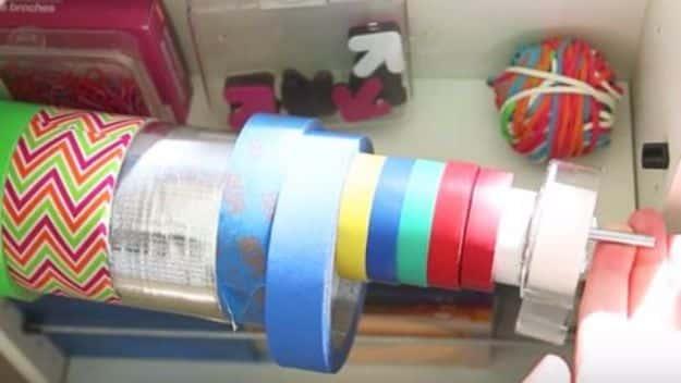 Shallow drawer with wooden dowels threaded through rolls of duct tape, washi and colored masking tape in rainbow order