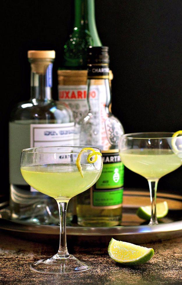 Two coupe glasses of pale green Last Word cocktail on a tray with gin and green Chartreuse bottles behind