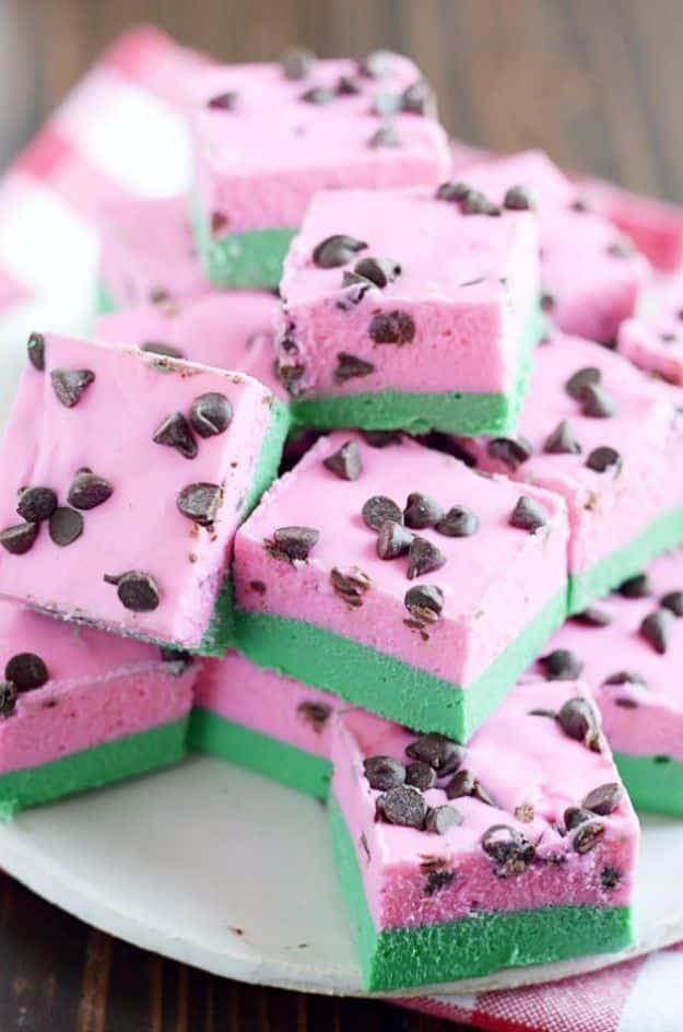 Stacked squares of pink and green watermelon fudge topped with mini chocolate chips standing in as seeds