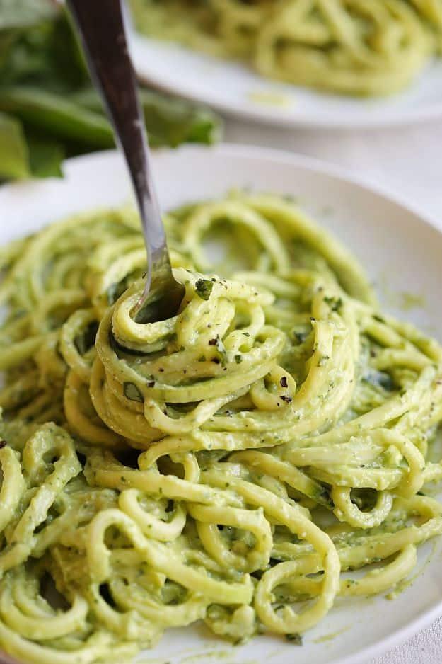 Zucchini noodles with creamy avocado pesto, green spiralized noodles twirled on a fork in a white bowl