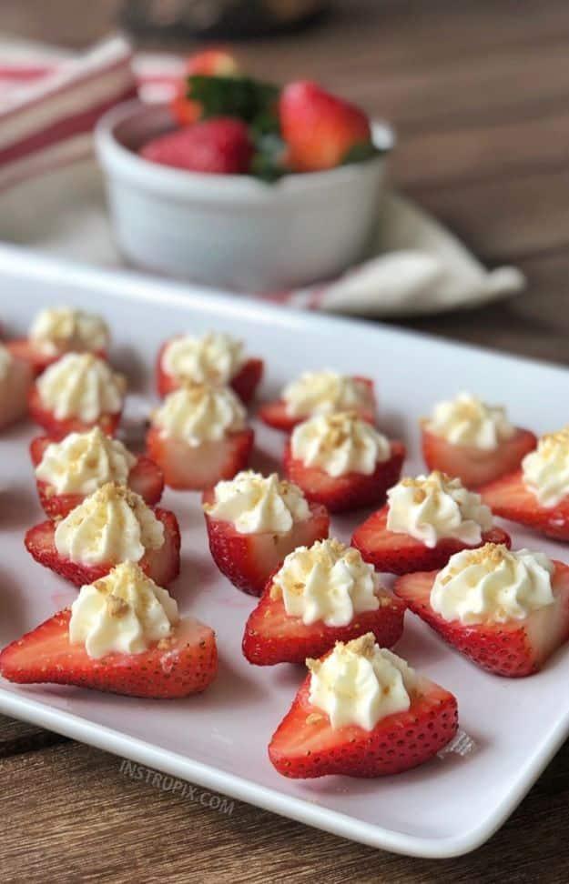 Deviled strawberries filled with piped cheesecake cream on a white rectangular platter with a bowl of berries