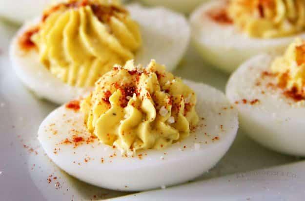 Traditional deviled eggs with piped yellow filling dusted with paprika arranged on a white serving plate