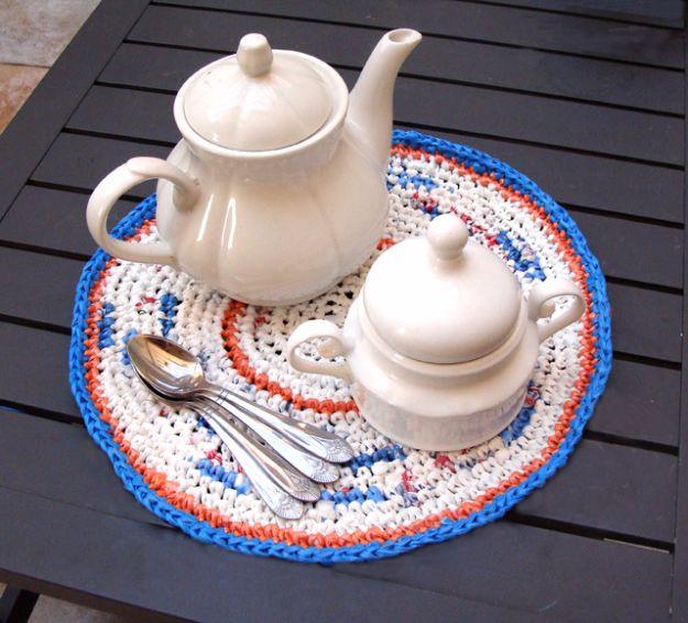Round crocheted plarn placemat in cream flecked with red and blue, edged in blue and orange, under a white teapot