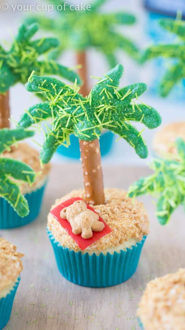 Palm tree cupcakes in teal liners with pretzel trunks, candy fronds and a teddy graham on a red towel