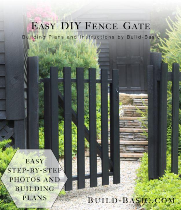 DIY fence gate, a narrow black painted picket gate hung between dark posts on a gravel path beside a hedge