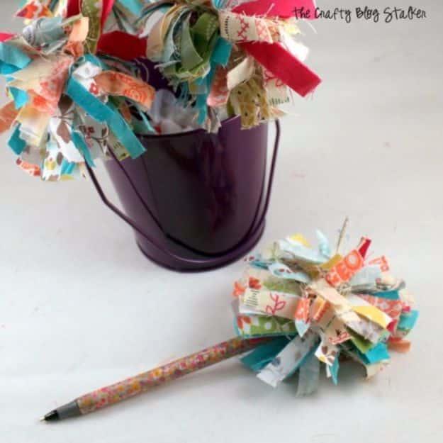 Quilting scraps pom pom pens in bright print fabric strips standing in a purple tin with one pen lying beside it