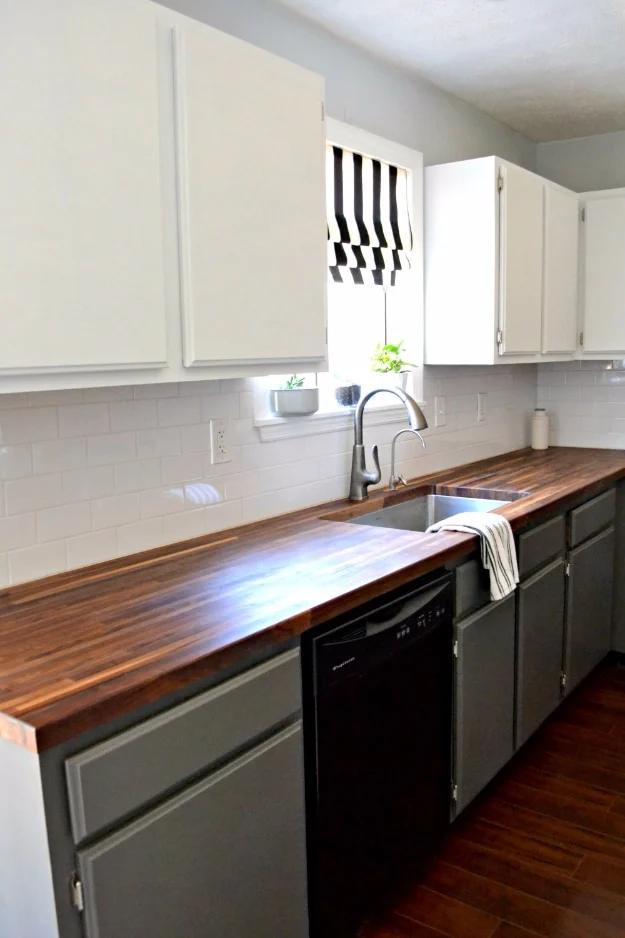 Kitchen with white upper cabinets, grey painted lower cabinets, dark walnut butcher block counter and white subway tile