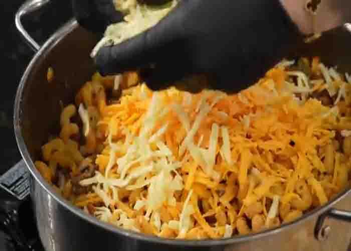 Adding the shredded cheese to the hamburger helper