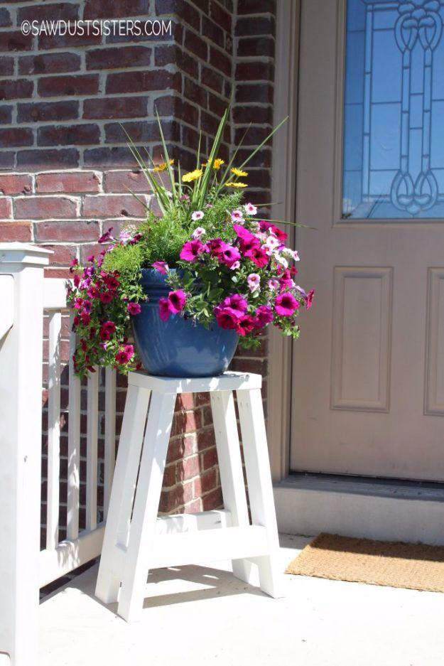 DIY bar stool made only from 2x4s painted white with splayed legs, used as a porch plant stand holding petunias