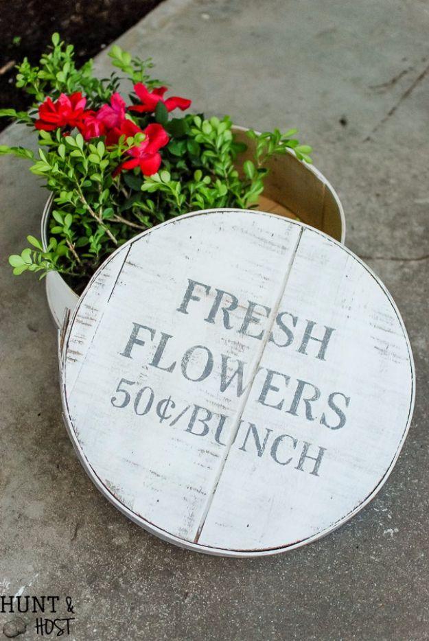 Round wood lid stenciled Fresh Flowers 50 cents a bunch leaning against a metal bucket of red blooms