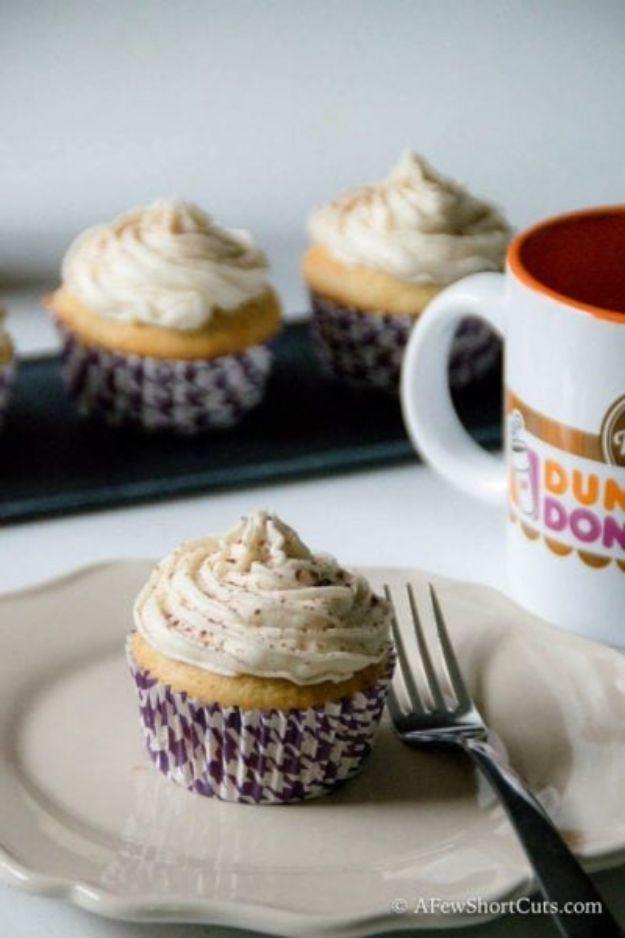 Vanilla latte cupcakes in purple liners with swirled coffee buttercream beside a Dunkin coffee mug on a plate