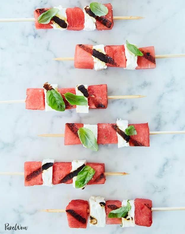 Grilled watermelon feta skewers with watermelon cubes, white feta and basil on wooden skewers over white marble