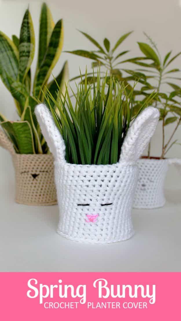 Bunny planter cover crocheted in white, with long ears and a stitched sleeping face, slipped over a pot of grass