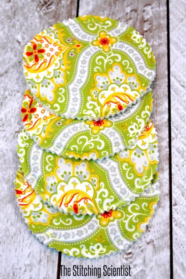 Four round green and yellow paisley fabric coasters with pinked edges stacked on weathered white wood boards