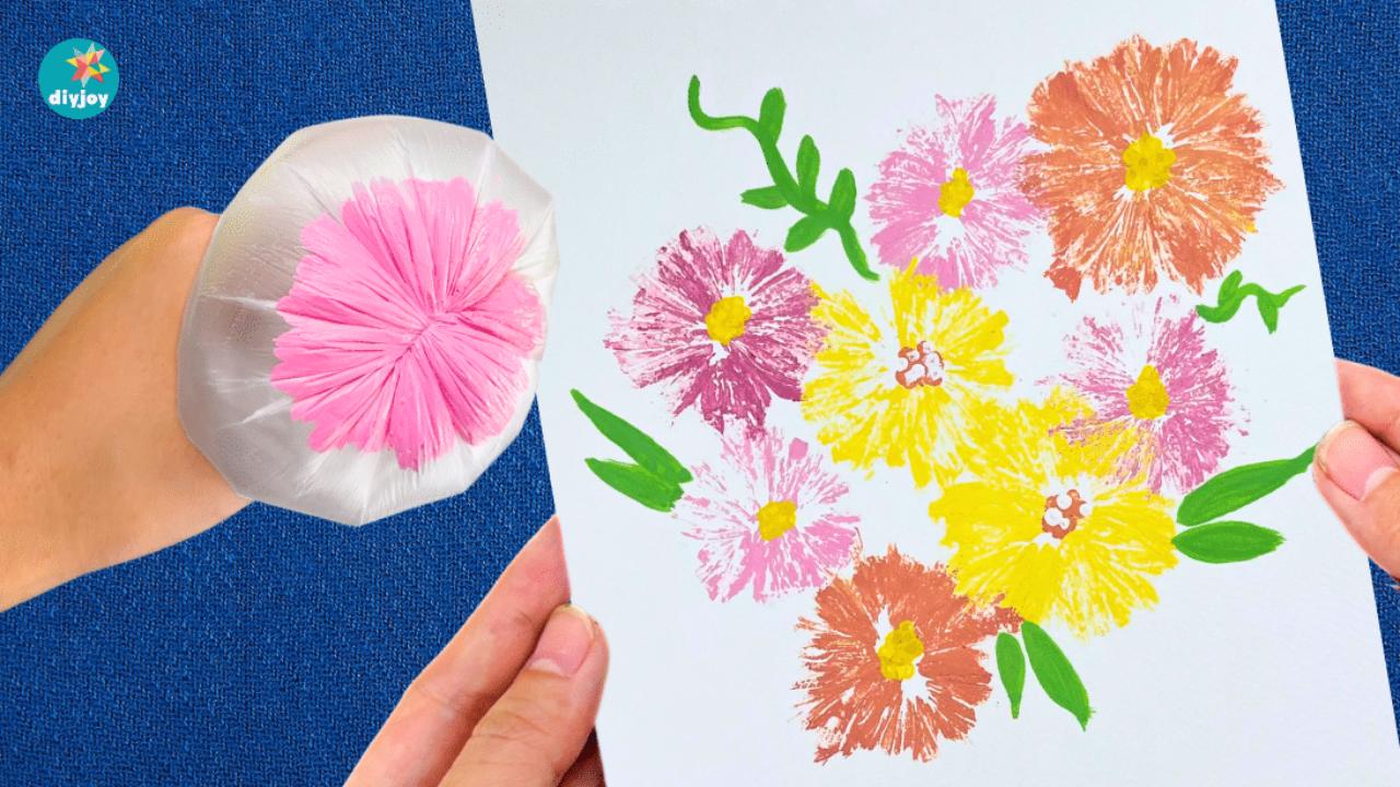 An inflated plastic bag loaded with pink paint beside a card of stamped flowers in pink, purple, yellow and orange