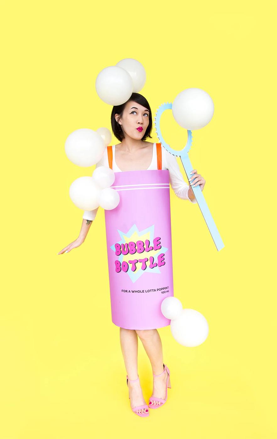 Adult wearing a pink bubble bottle costume with white balloon bubbles and holding a cardboard bubble wand
