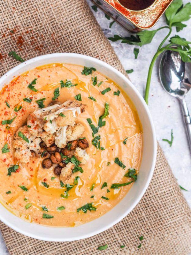 Roasted cauliflower soup in a white bowl with a swirl of paprika, chopped herbs and a toasted crunchy topping