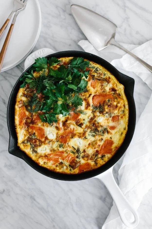 Smoked salmon frittata in a cast iron skillet with goat cheese, fresh dill and leeks, cut into wedges