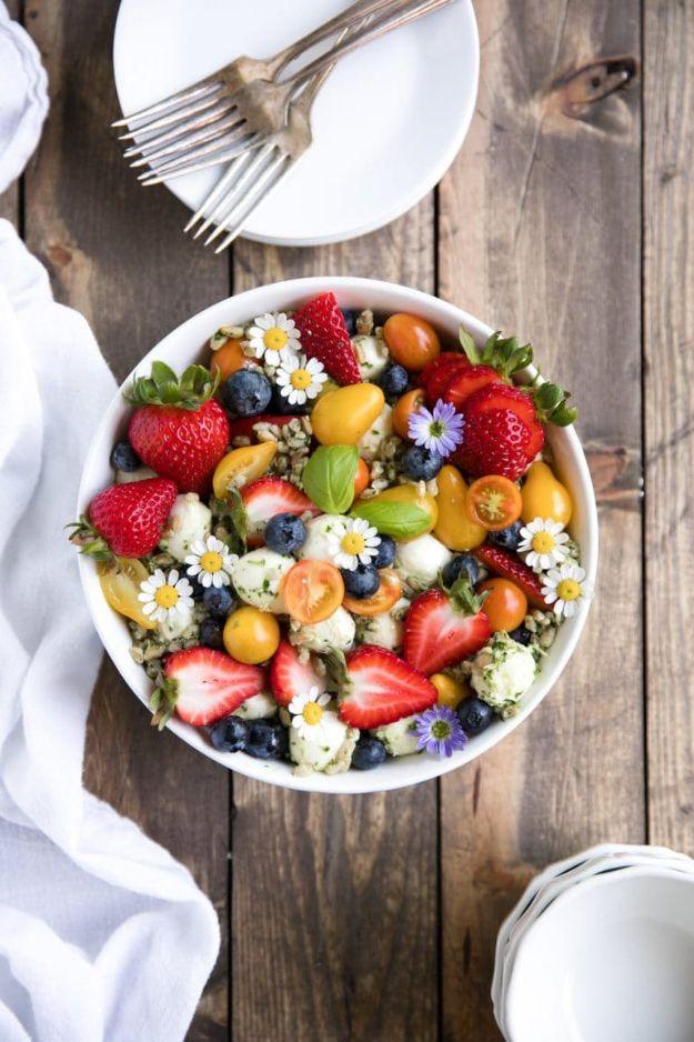 Strawberry and blueberry caprese farro salad in a white bowl with mozzarella pearls and edible flowers on wood