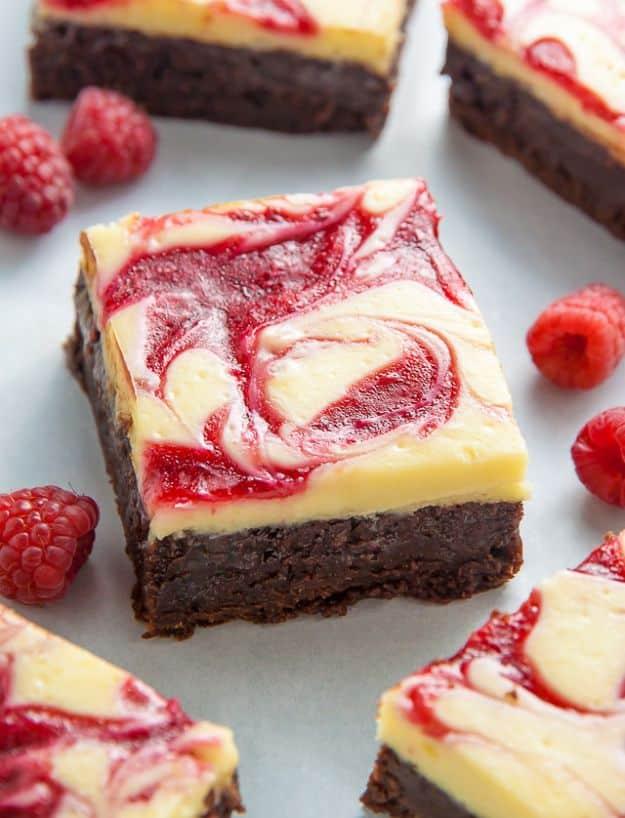 White chocolate raspberry cheesecake brownies with pink swirled topping and fresh raspberries scattered around