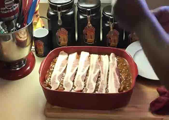 Laying the slices of bacon on top of the beans