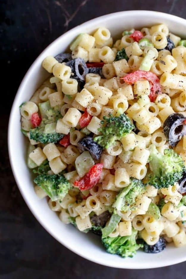 Creamy pasta salad in a white bowl with small macaroni, broccoli florets, red pepper and sliced black olives
