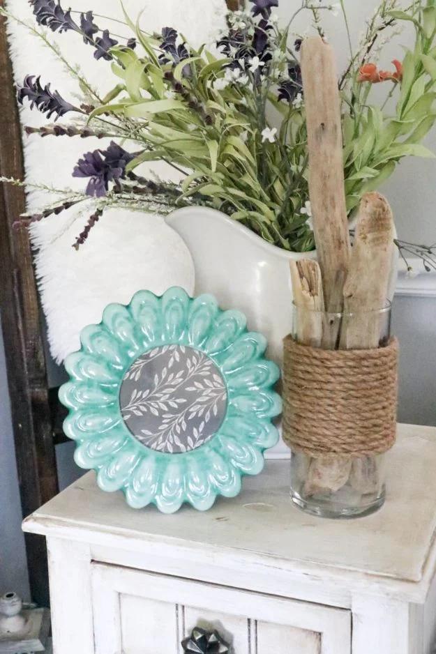 Rope wrapped hurricane vase with driftwood and dried purple flowers beside a teal dish on white wood