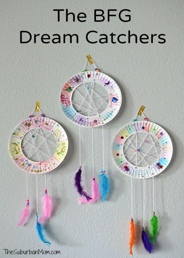 Three paper plate dream catchers with yarn webs, sequins and pink, purple and green feathers hanging on a gray wall