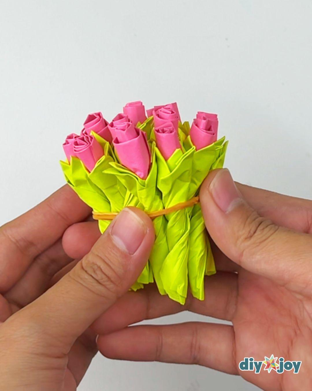 Two hands gathering a small bunch of finished pink paper roses made from Post-it notes into a bouquet