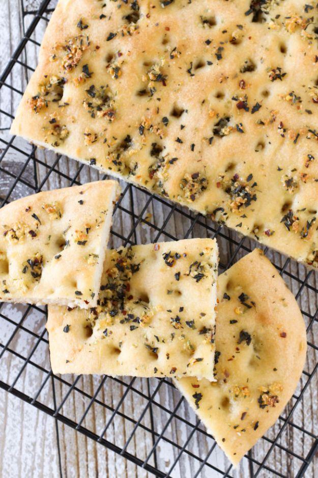 Squares of gluten free herb focaccia flecked with dried oregano and basil cooling on a black wire rack