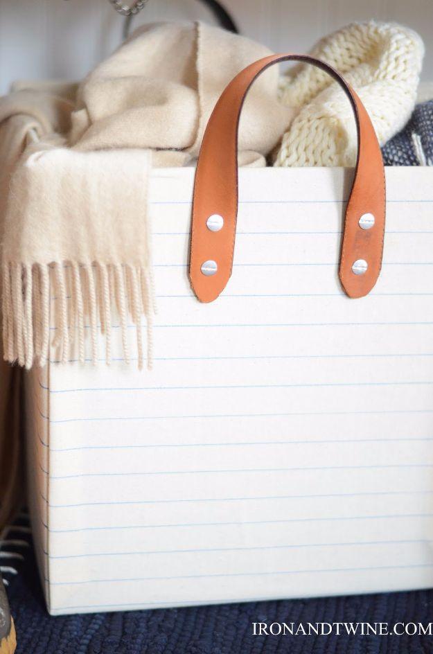 Cardboard craft storage bin covered in pale striped fabric with tan leather belt handles holding blankets