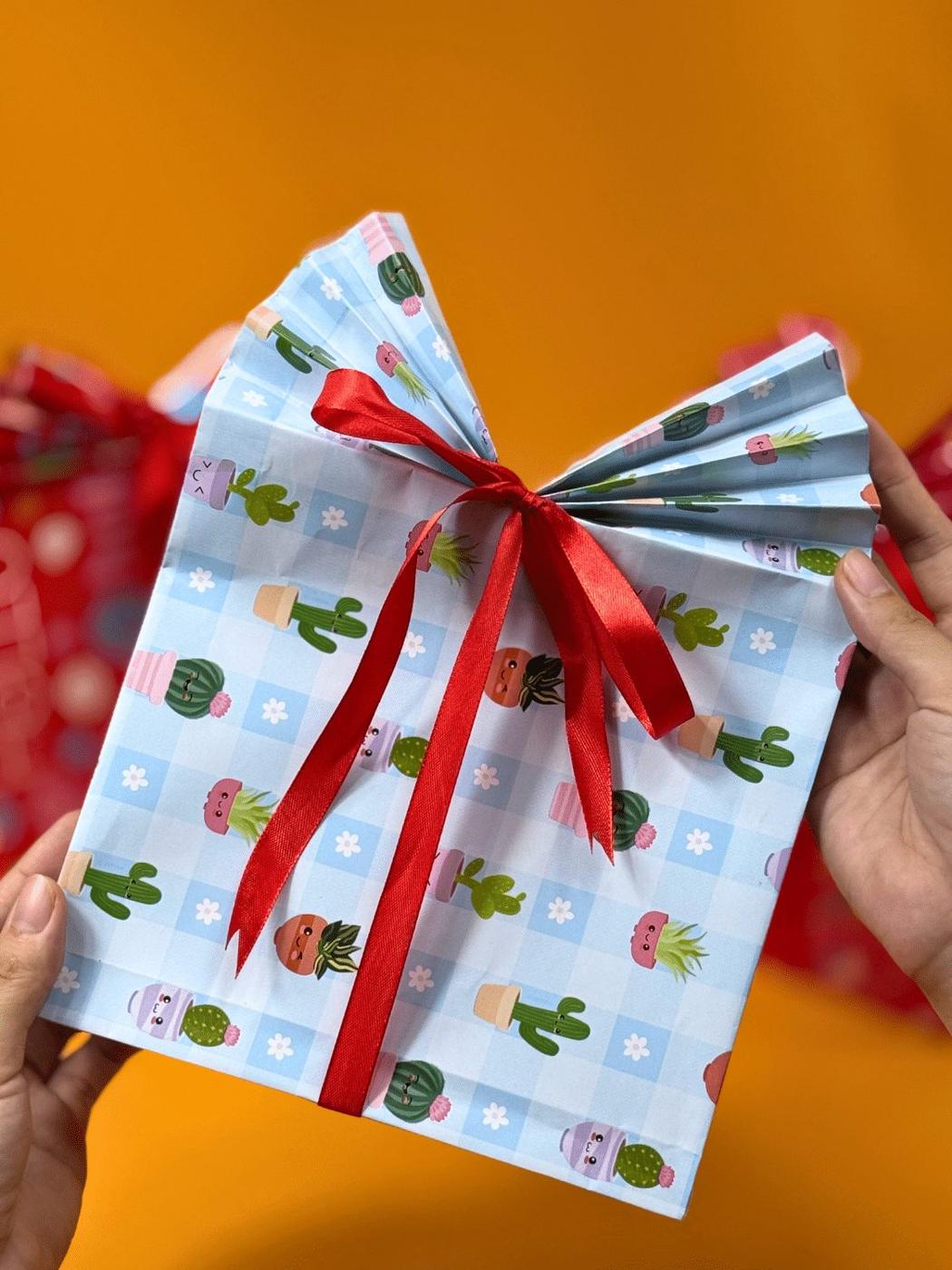 A handmade gift bag folded from a flat sheet of patterned wrapping paper with a pleated top and ribbon