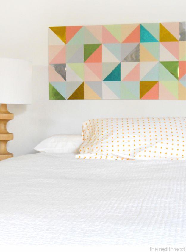 Wide patchwork panel of paper triangles in mint, coral, mustard and gray hanging above a white bed with a lamp