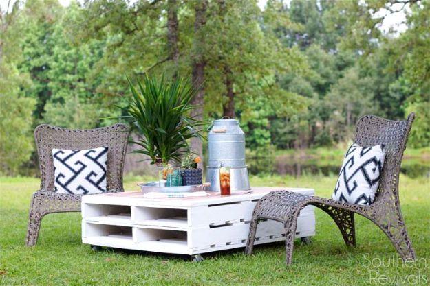 DIY pallet outdoor coffee table painted white with a planked top, on grass between two woven patio chairs