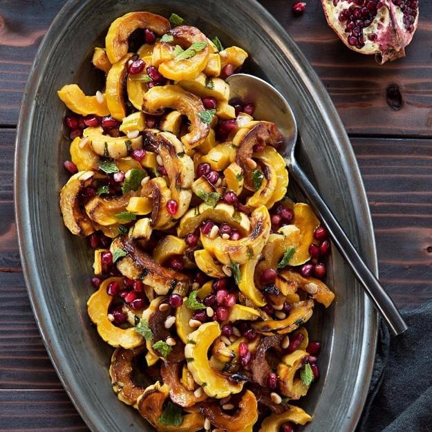 Honey glazed roasted delicata squash rings on a platter with pomegranate seeds, pine nuts and fresh mint
