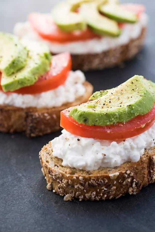 Avocado toast with cottage cheese, two slices of seeded toast topped with sliced tomato and avocado wedges