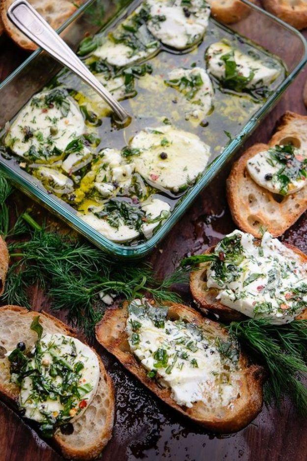Herbed goat cheese in a glass baking dish with fresh dill and oil, beside baguette slices spread with it