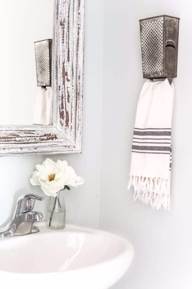 A vintage metal box grater mounted on a stained board holds a striped kitchen towel on its small hook