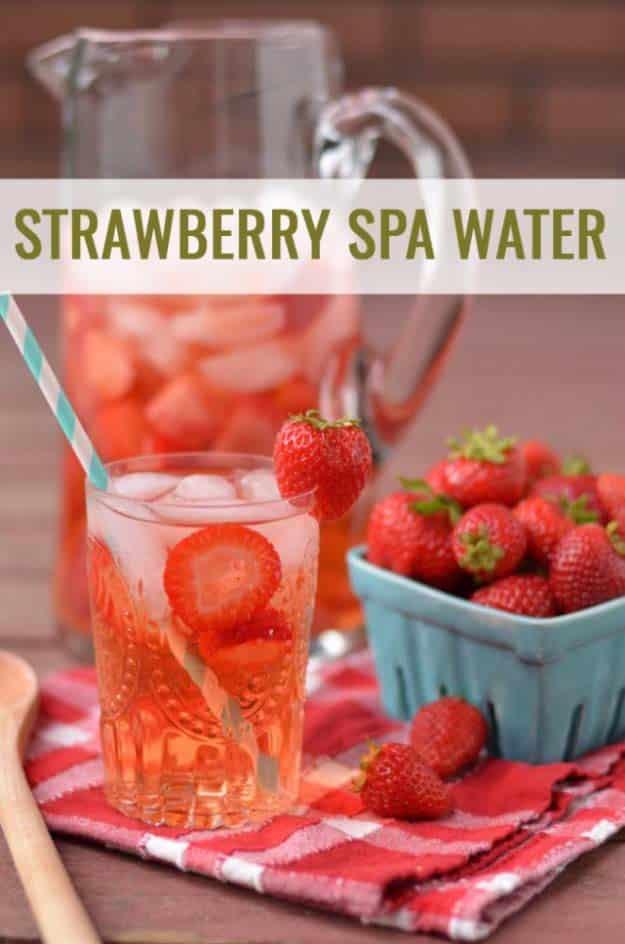 Strawberry spa water in a glass pitcher and glass with halved strawberries beside a blue basket of berries