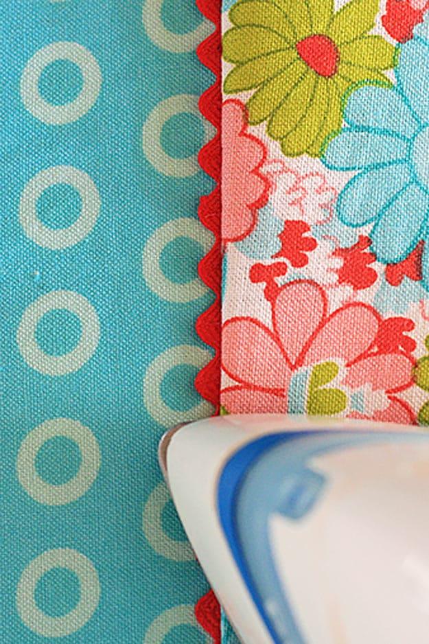 Add any trim to a seam without pins, a hand pressing a folded strip of patterned fabric being stitched along a marked seam
