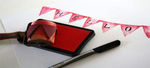Wooden roller stamp and a red ink pad beside a printed pink pennant bunting stamped across white paper reading hello