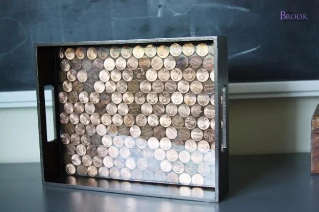 Penny tray with black handles filled with mixed coins under a glossy resin pour, standing against a chalkboard