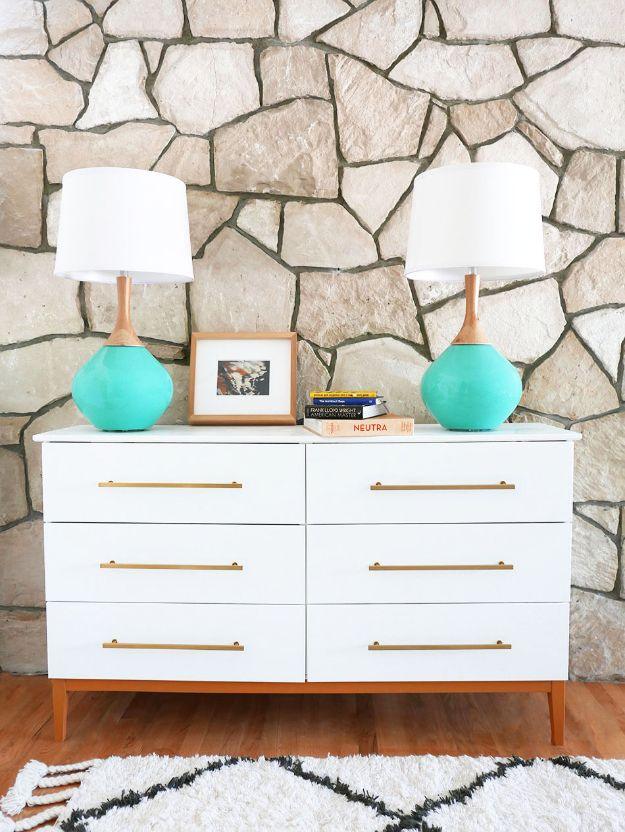 White IKEA Tarva dresser hacked midcentury with six long brass pulls and wood legs, teal lamps against a stone wall