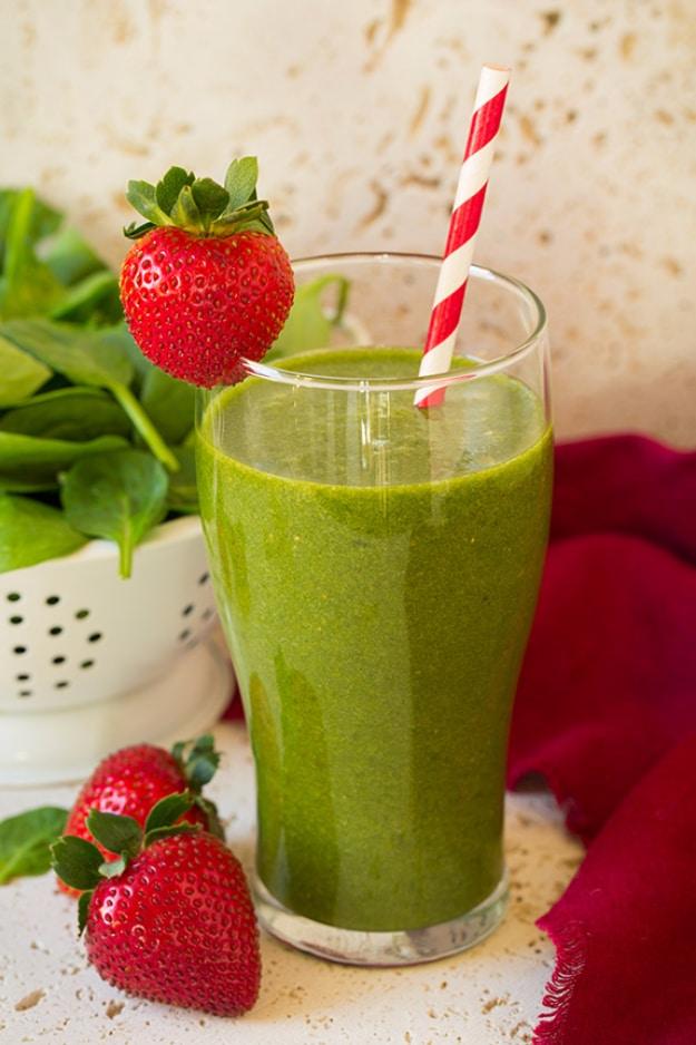 Bright green strawberry spinach smoothie in a tall glass with a red striped straw and a strawberry on the rim