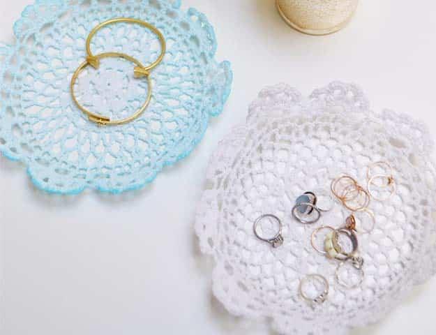 Lace doily jewelry holders, two stiffened doily dishes, one pale blue holding gold hoops and one white holding rings