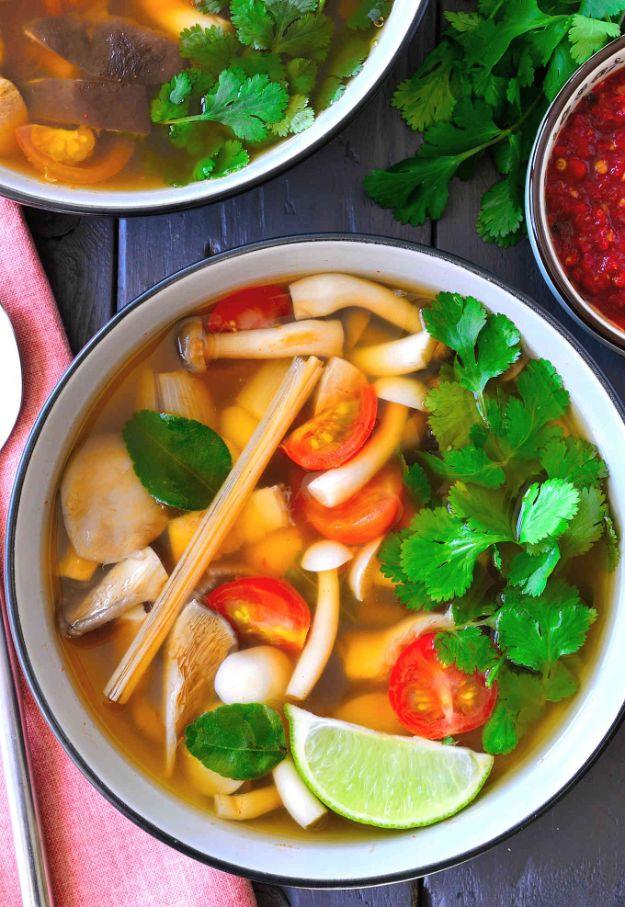 Vegetarian tom yum soup in a white bowl with mushrooms, lemongrass stalks, cherry tomatoes, lime and cilantro