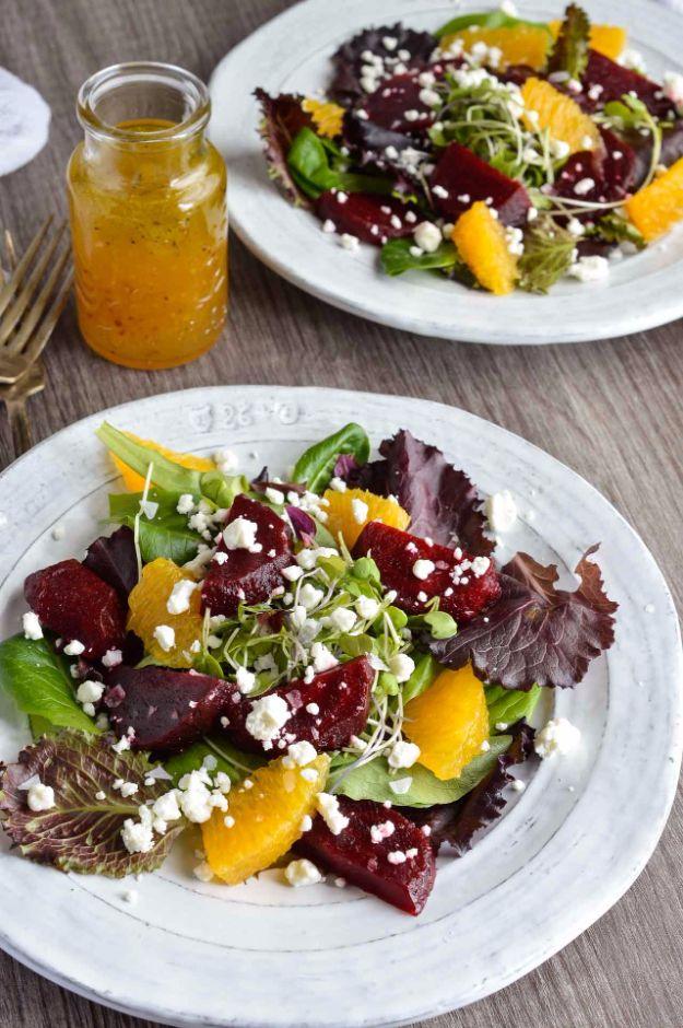 Beet salad with dark red beet chunks, orange segments and white goat cheese crumbles on greens with micro greens