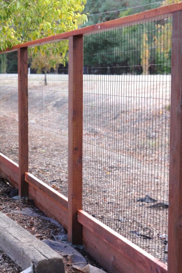 Deer fence, fine black mesh fencing stretched on dark stained wooden posts along a driveway edge with trees behind