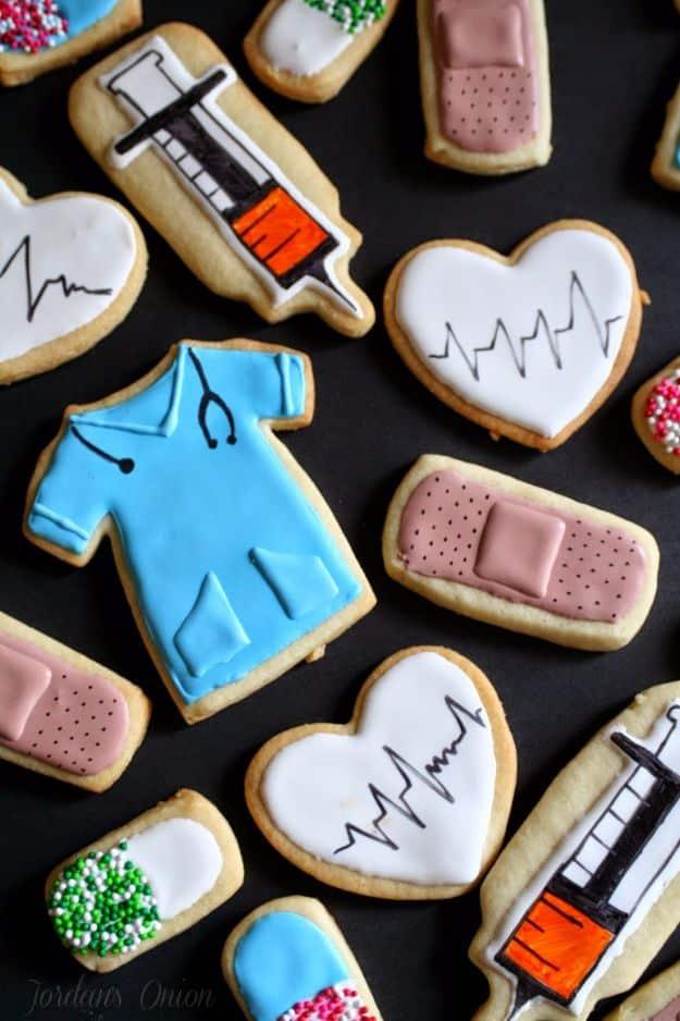 Nursing graduation cookies iced as blue scrubs, syringes, bandages and white hearts with an EKG line across them